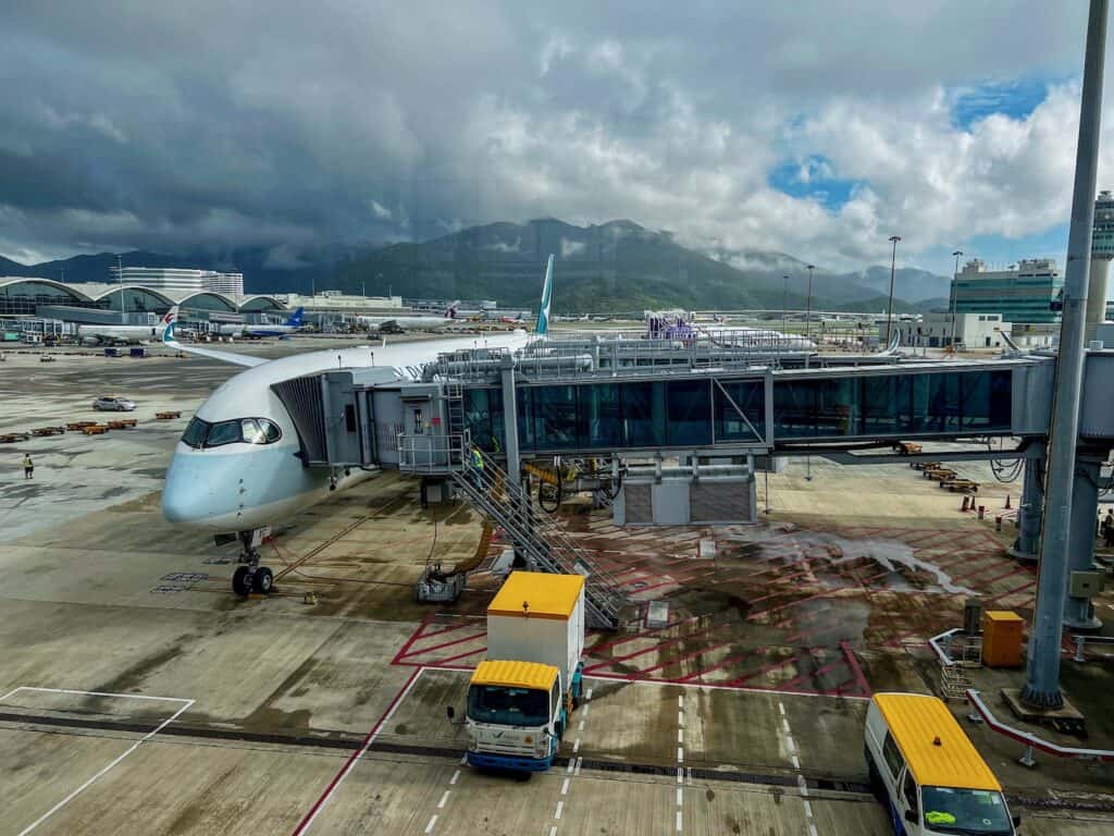 View out of Hong Kong airport window looking at a plane at the gate and green mountains in the background